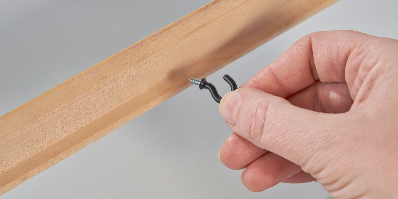 Una mano avvita un gancio alla parte interna di una cornice di legno.