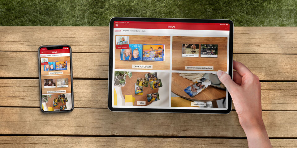 Jemand hält ein Tablet und betrachtet digitale Fotobücher auf einem Tisch, dazu ein Smartphone.