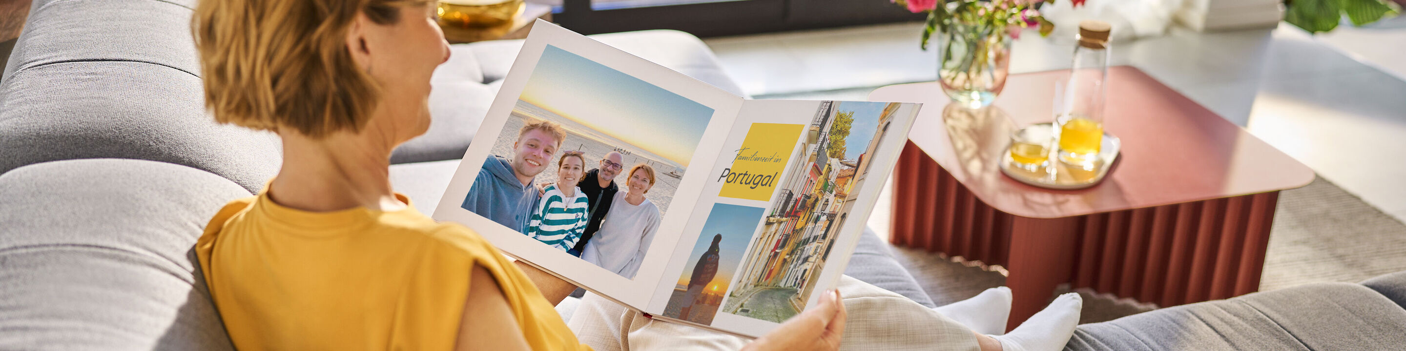 Eine Person sitzt auf der Couch und schaut ein Fotobuch mit Urlaubsbildern an