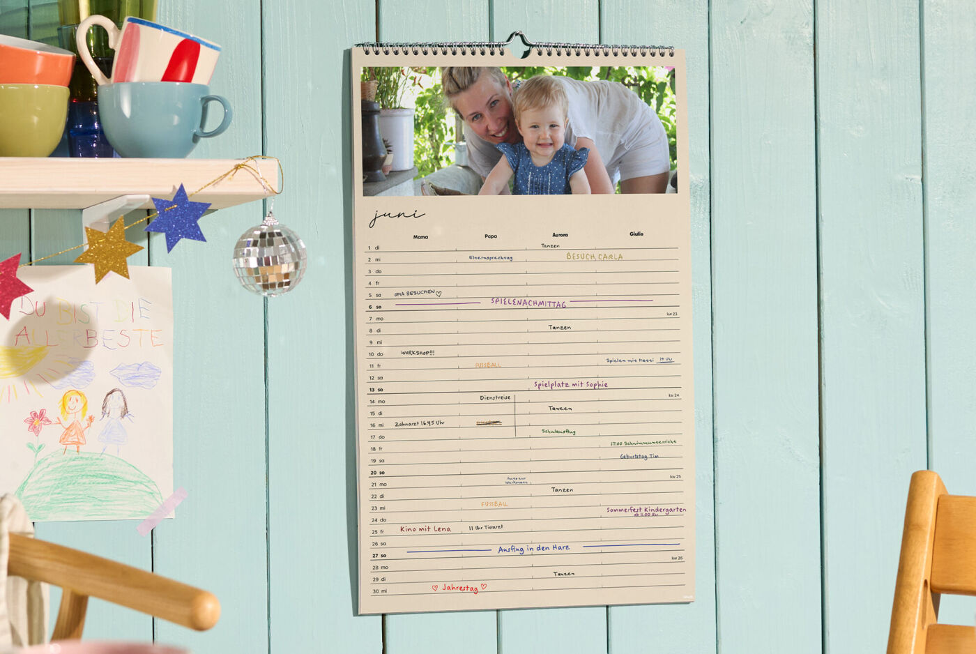 CEWE-Fotokalender als Familienplaner hängt an der Wand, Monat Juni mit Terminen und Foto oben sichtbar